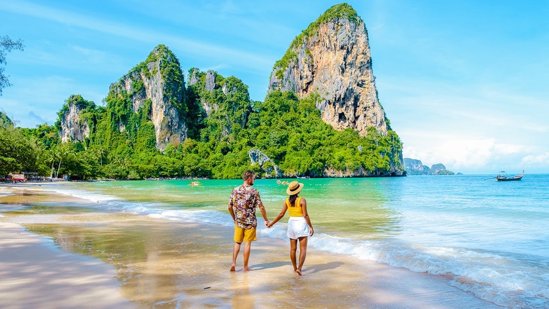 Couple walking on Railay Beach with limestone cliffs in Krabi, Thailand.