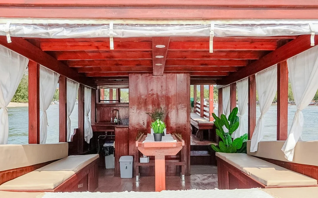 Interiors of a long tail boat in Krabi with wooden seating and potted plants.