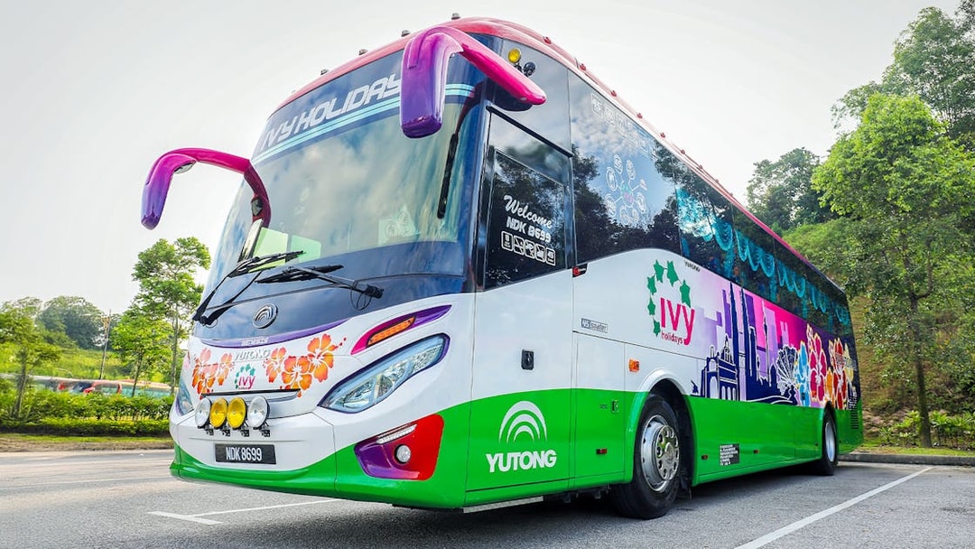 Colorful tour bus for transfers to Genting Highlands parked on a scenic road.