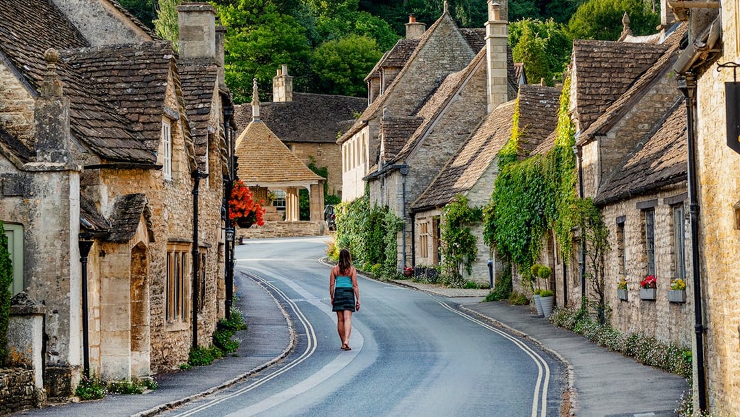 Tourist walking through a picturesque village street in the Cotswolds, England.