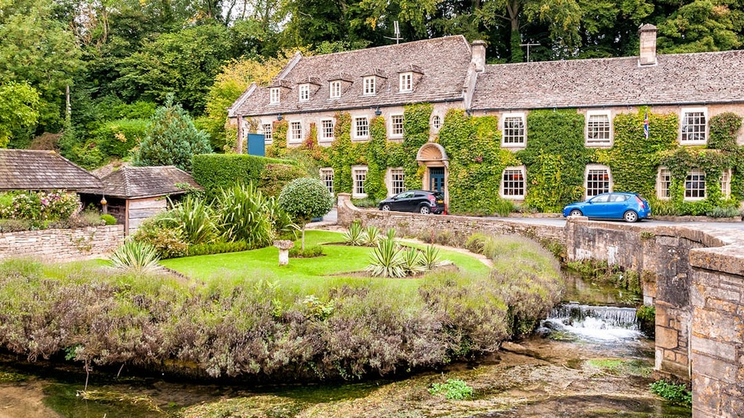 Cotswolds stone house with ivy, garden, and stream on a London day tour.