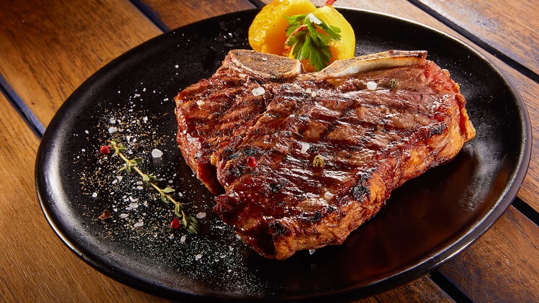 Grilled beef steak with rosemary on a black plate.