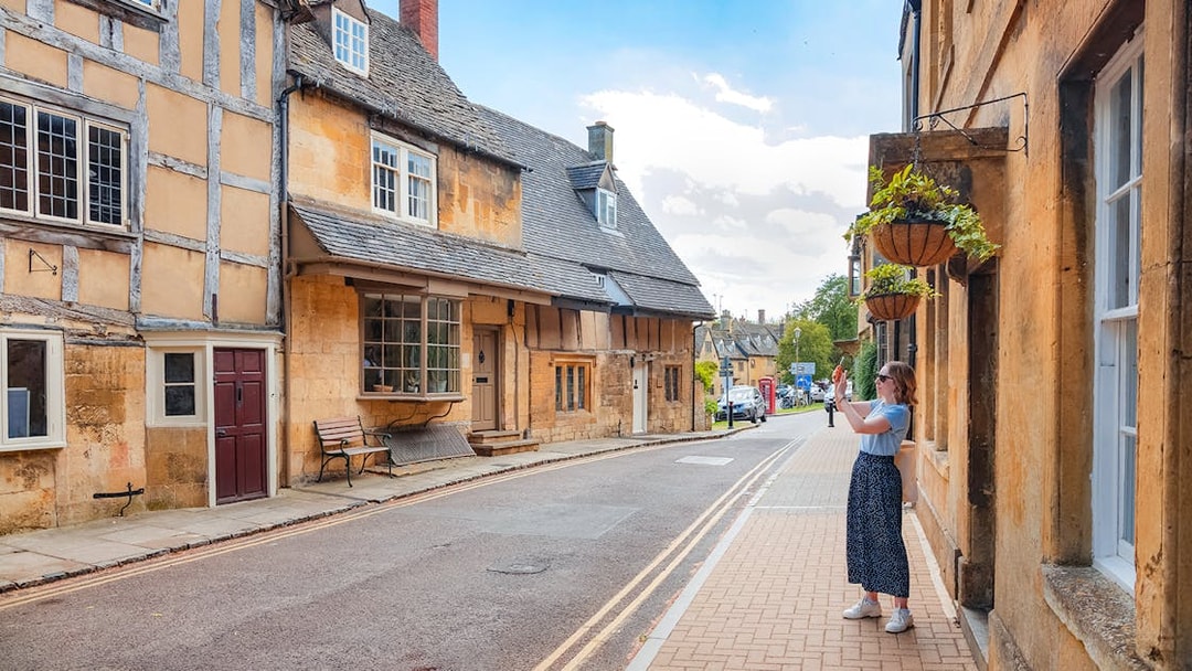 Cotswolds street scene with historic buildings and a person taking photos.