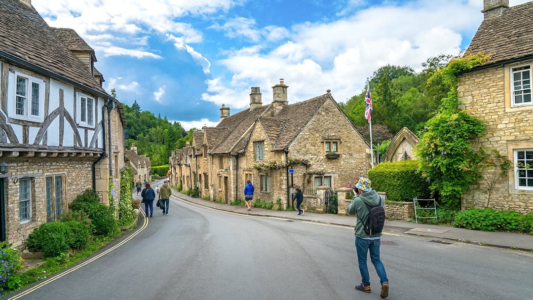 Quaint street in Castle Combe village, Cotswold, with historic stone cottages and visitors exploring.