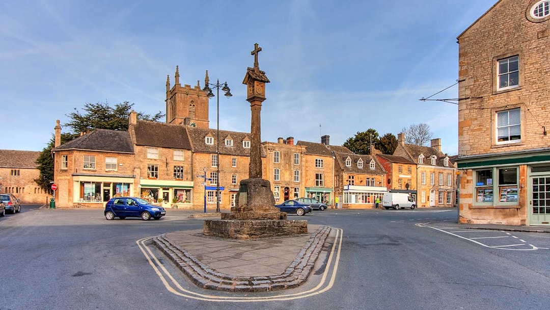 Cotswolds village square with historic stone buildings and market cross.