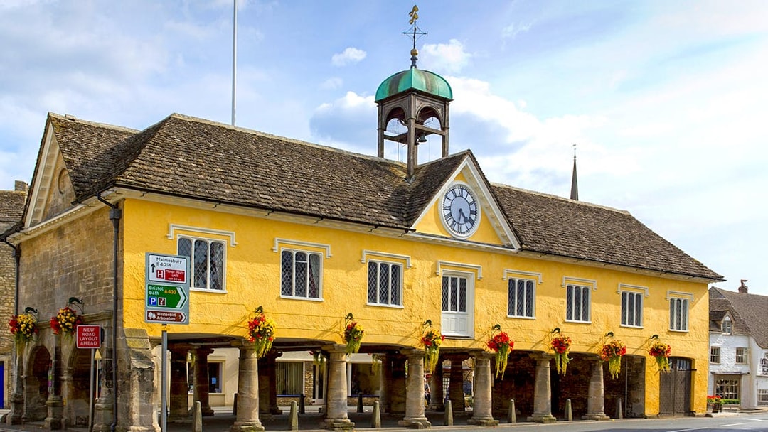 Historic market hall in Cotswolds with clock tower and floral decorations.