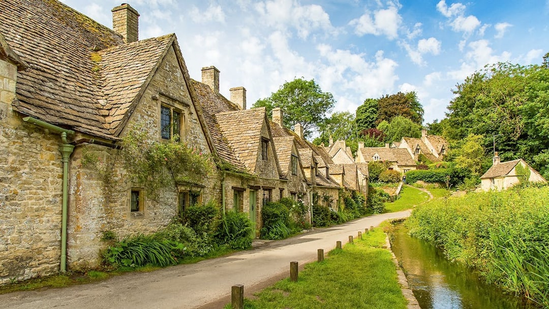 Cotswolds stone cottages along a narrow road with lush greenery, part of a guided day tour from London.