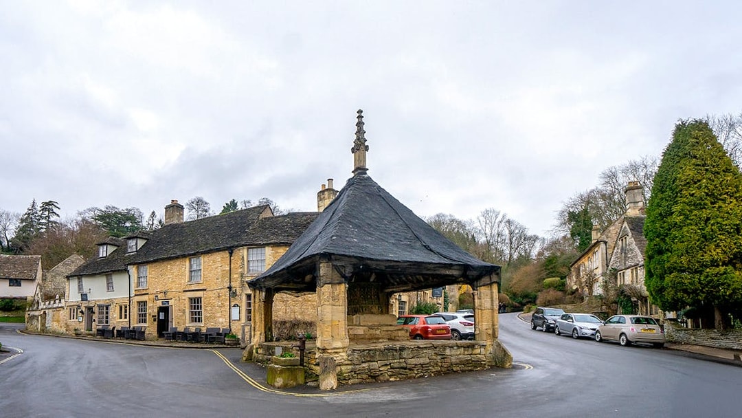 Cotswolds village scene with historic market hall and stone cottages.