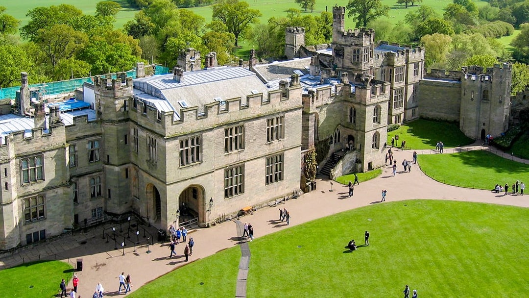 Aerial view of Warwick Castle with visitors walking on the grounds, surrounded by lush greenery.