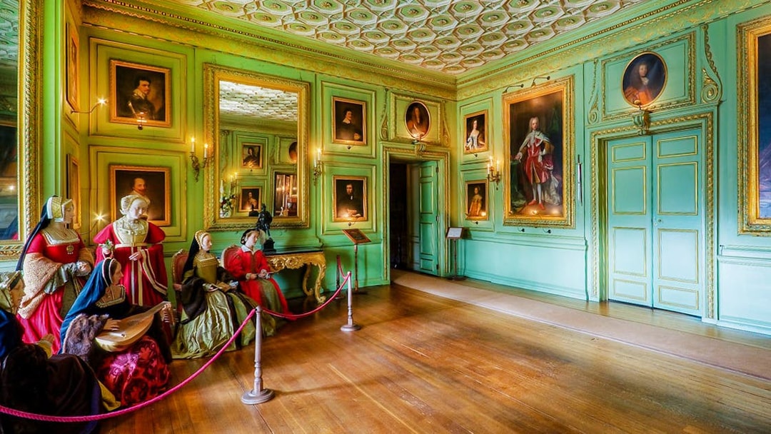 Warwick Castle interior with historical figures and portraits on green walls.