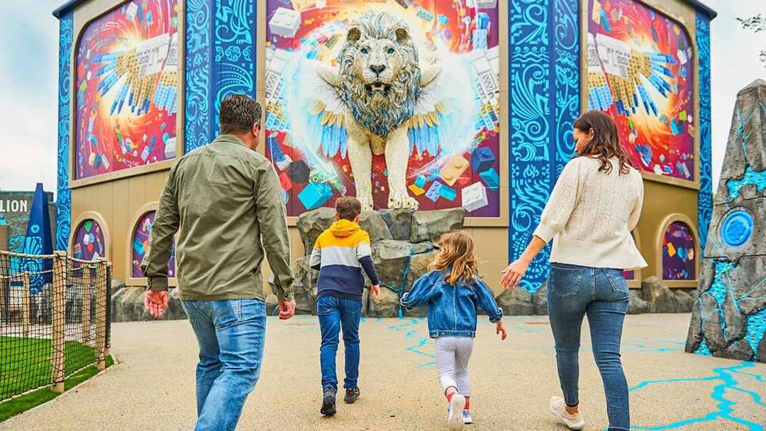 Family approaching a colorful LEGO lion mural at a theme park.