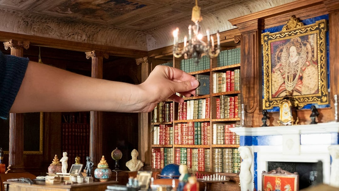 Hand arranging miniature books in Windsor Castle library model.