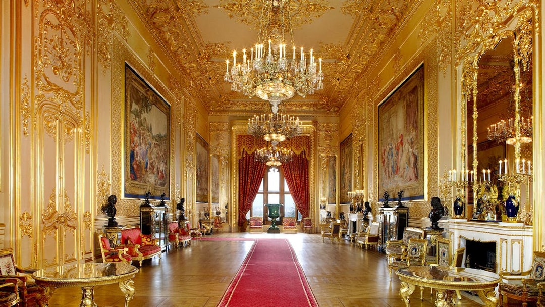 Windsor Castle interior with ornate chandeliers, gilded walls, and red carpet.
