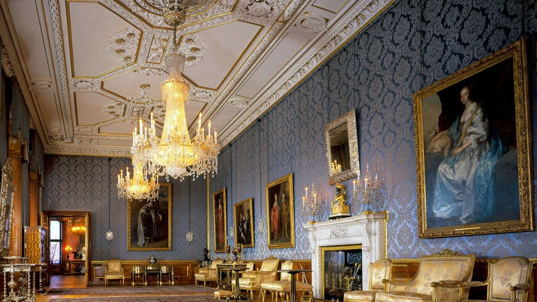 Windsor Castle interior with ornate chandeliers, blue damask walls, and classic paintings.