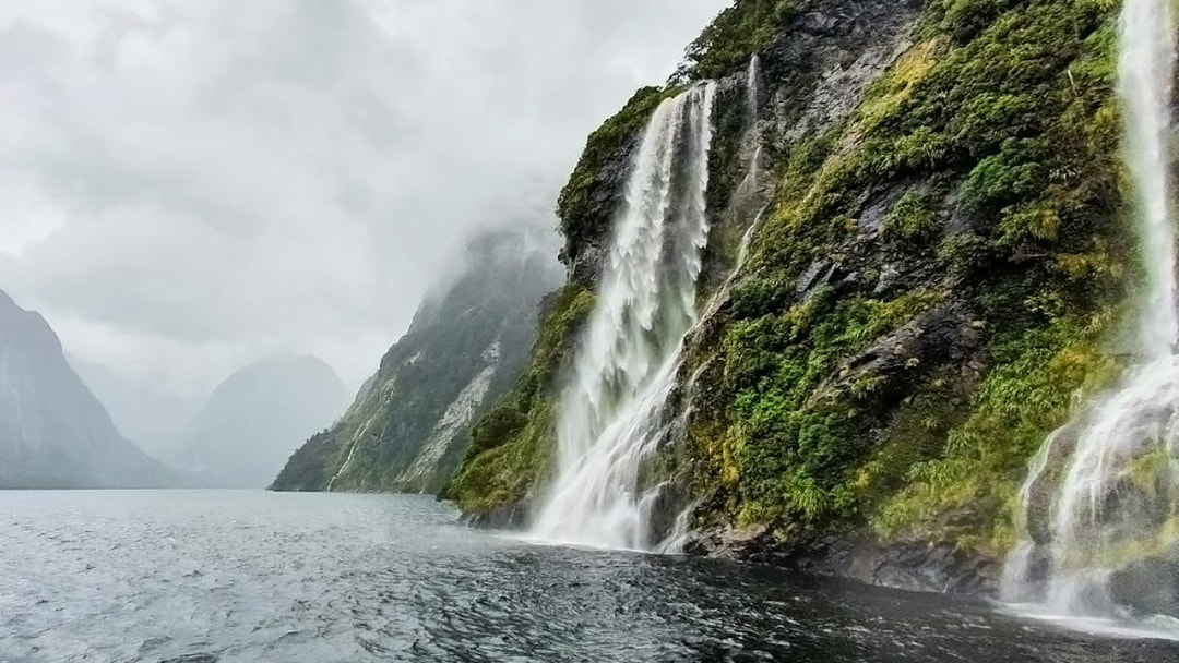 Waterfalls cascading down lush cliffs in Doubtful Sound, New Zealand, viewed from a cruise.