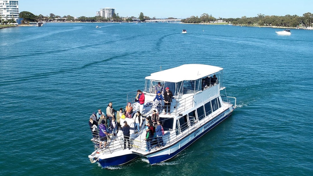 Tourists on a cruise boat in a scenic waterway with distant city skyline.
