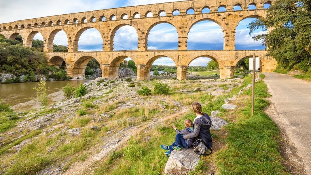 Pont du Gard aqueduct in Provence with a person and child sitting nearby.