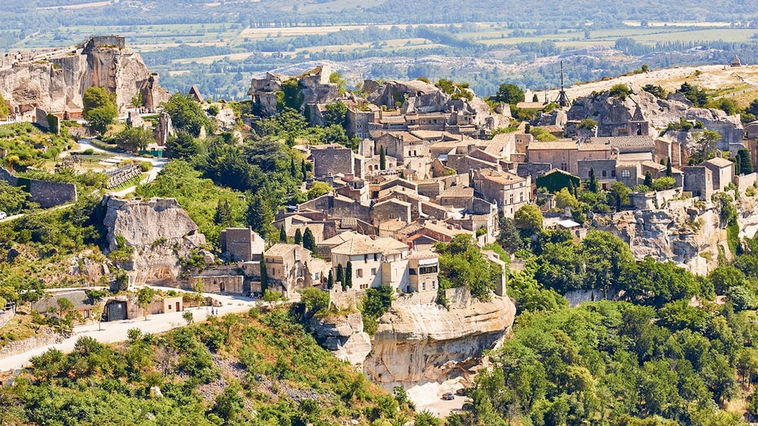 Hilltop village of Les Baux-de-Provence with stone buildings and lush greenery, Provence tour.