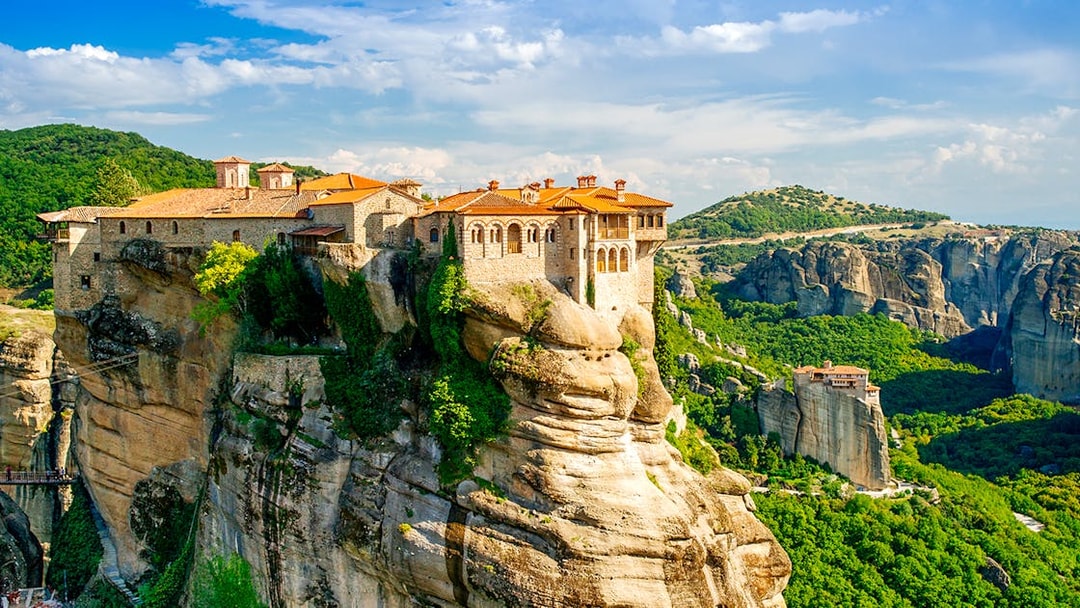 Meteora monastery perched on a rock formation in Greece, surrounded by lush green landscape.
