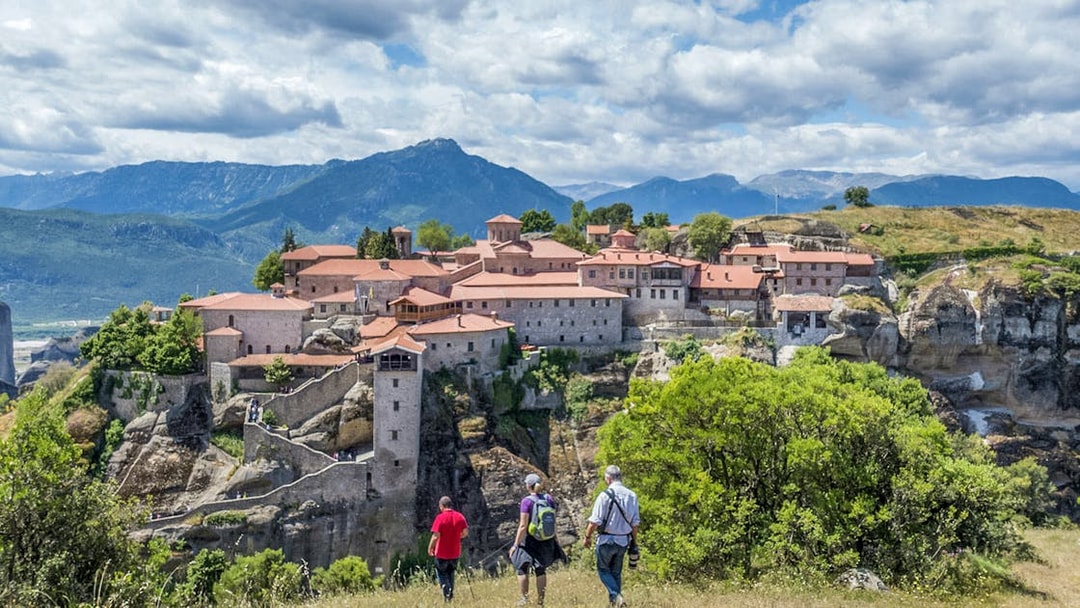 Guests hiking towards Meteora monastery with mountain backdrop.