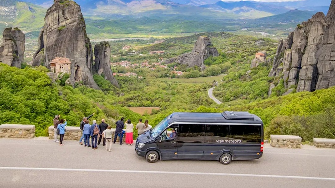 Tour group viewing Meteora rock formations and monastery during guided hiking transfer.