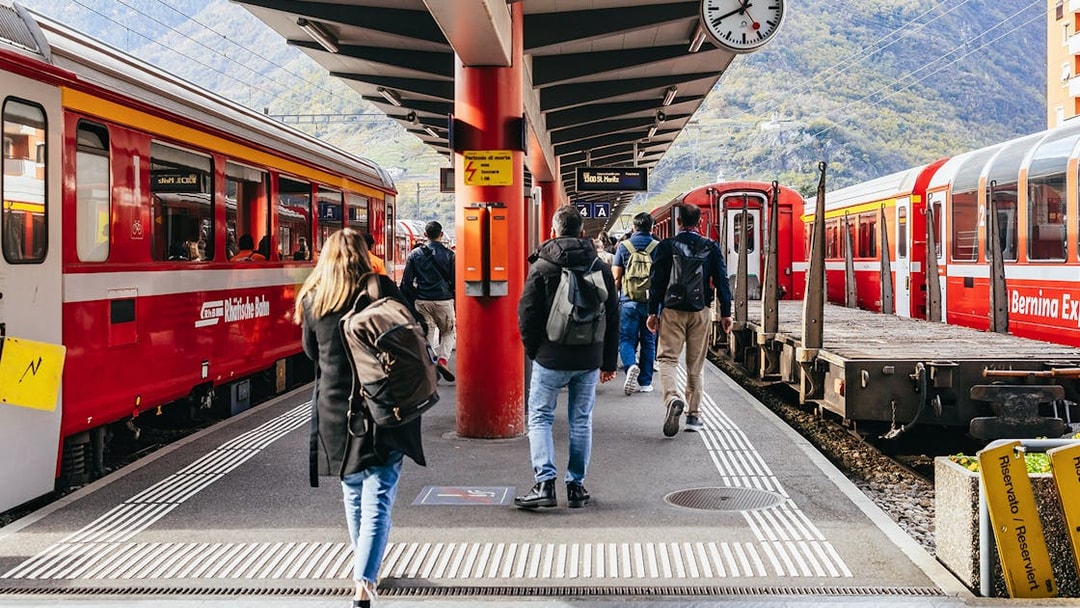 Travelers boarding the Bernina Red Train at a station in St. Moritz, surrounded by mountains.