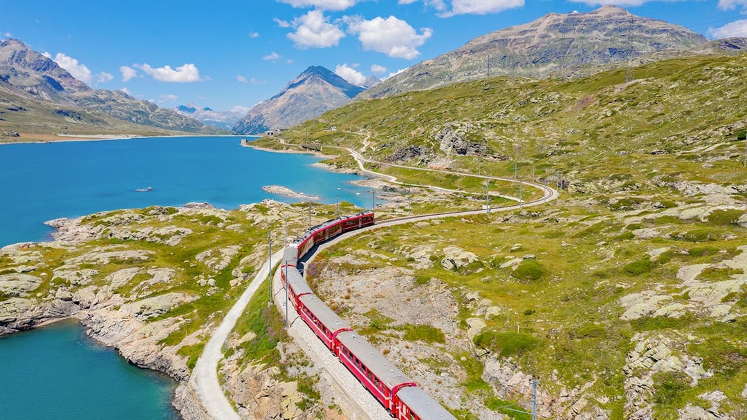 Bernina train traveling through Bernina Pass with lake and mountains in summer.