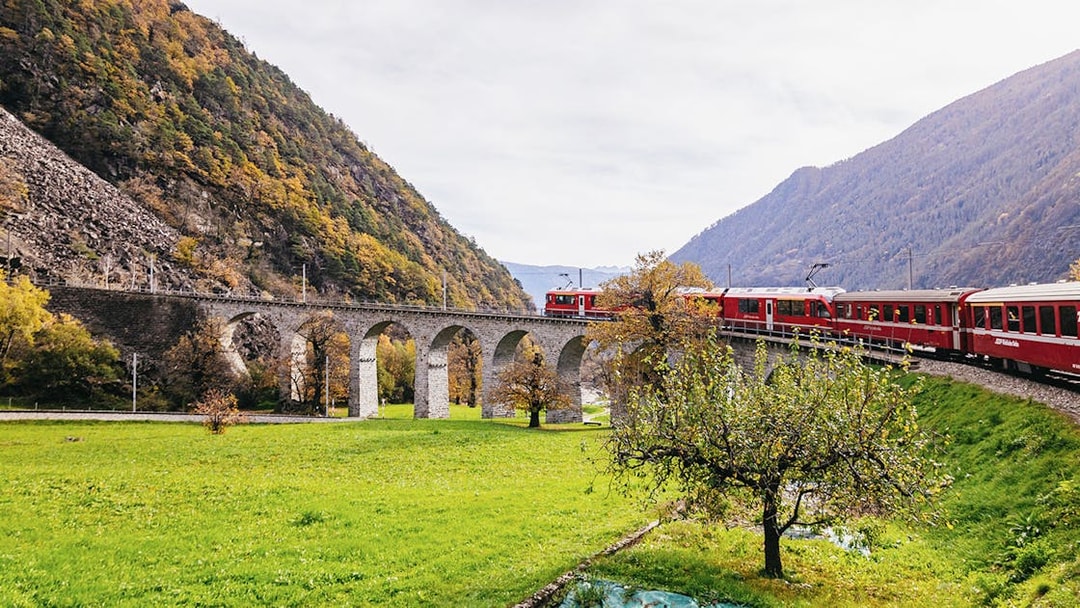 Bernina Red Train crossing a stone viaduct in a scenic valley near St. Moritz.