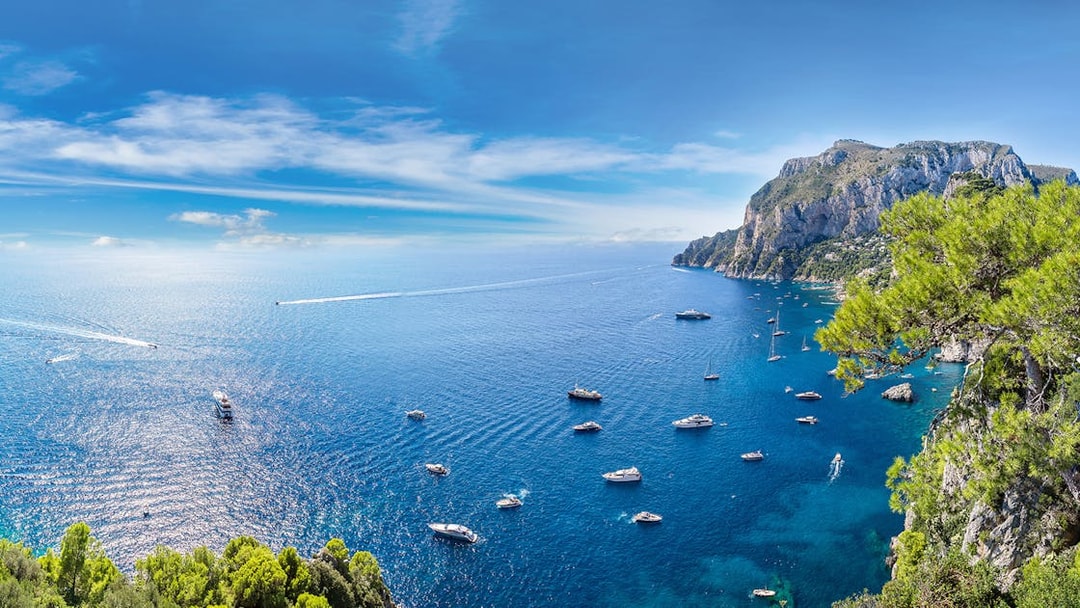 Boats in the blue waters near Capri with cliffs and greenery, view from Pompeii.