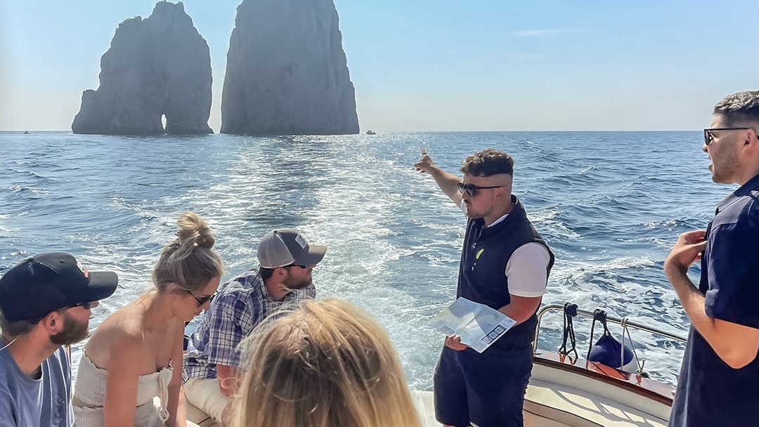 Tour group on a boat near Faraglioni rocks, Capri, with guide explaining the sights.