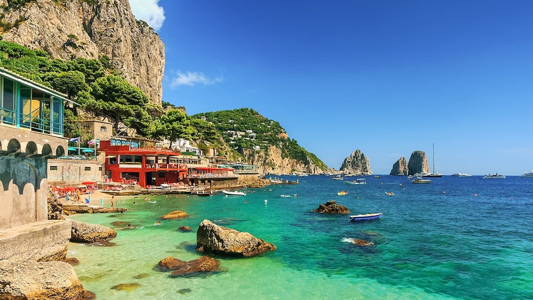 Capri coastline with Faraglioni rocks and boats, part of all-inclusive tour from Pompeii or Naples.