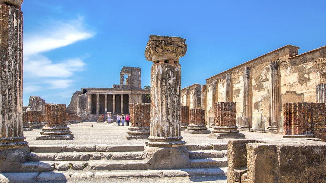 Ancient ruins of Pompeii with columns and Mount Vesuvius in the background.