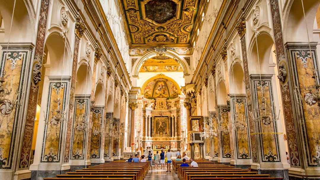 Interior of a historic church in Amalfi with ornate ceiling and visitors exploring.
