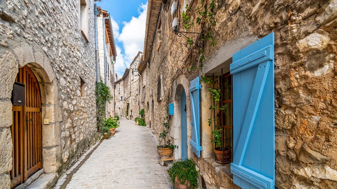 Narrow cobblestone street in a Provence village with stone houses and blue shutters.