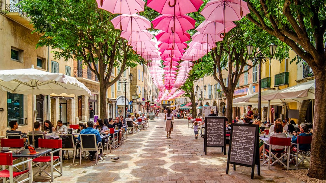 Street in Provence with pink umbrellas overhead and outdoor cafes.