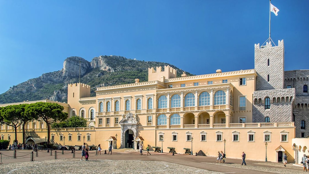Tourists exploring the Prince's Palace of Monaco with mountain backdrop on a French Riviera tour.