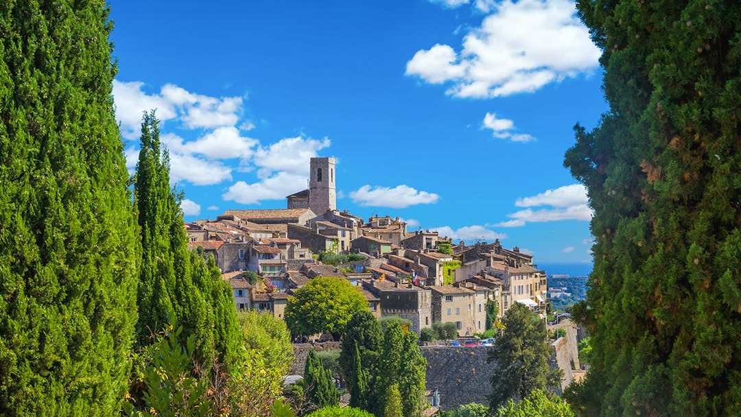 Hilltop village in the French Riviera with stone buildings and a church tower, surrounded by greenery.