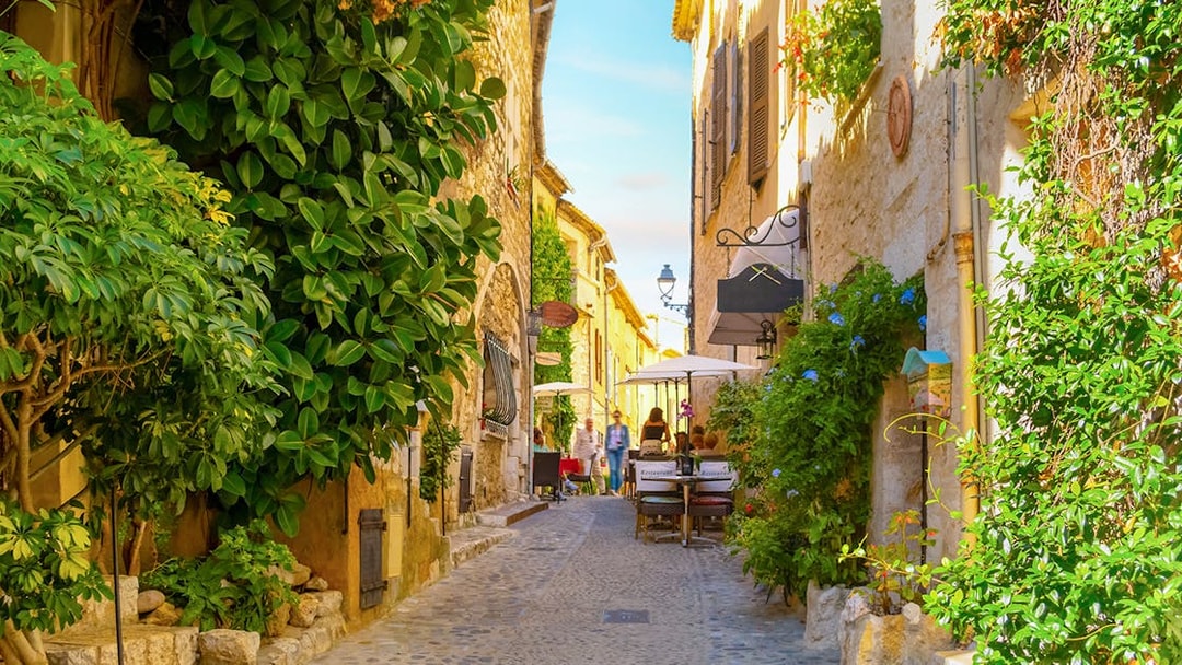 Cobblestone street with cafes and greenery in Saint Paul de Vence, France.