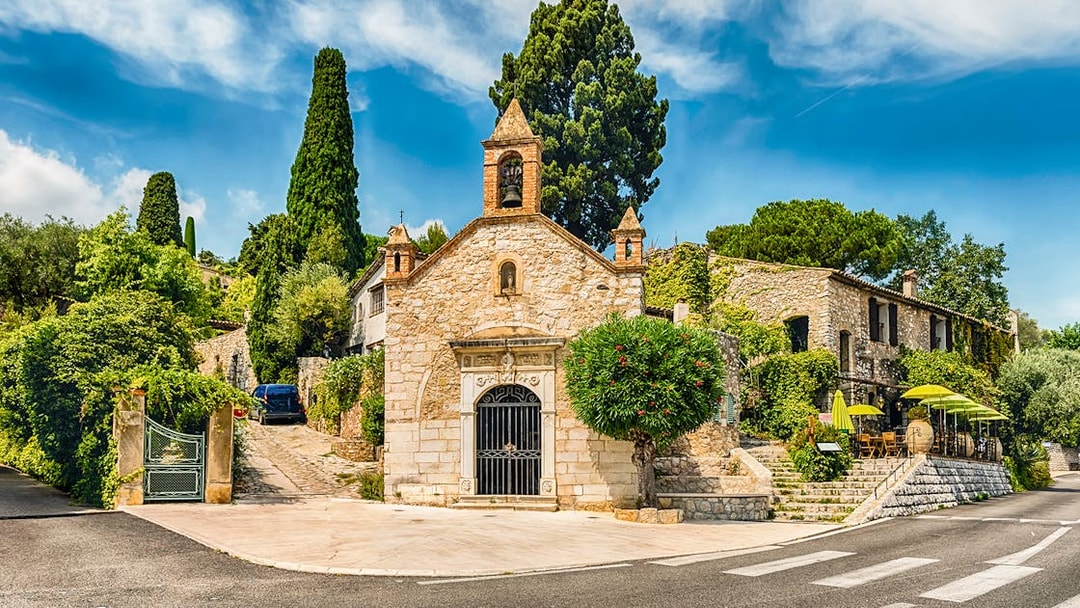 Stone chapel and cafe with green umbrellas on a French Riviera street, Nice day tour.