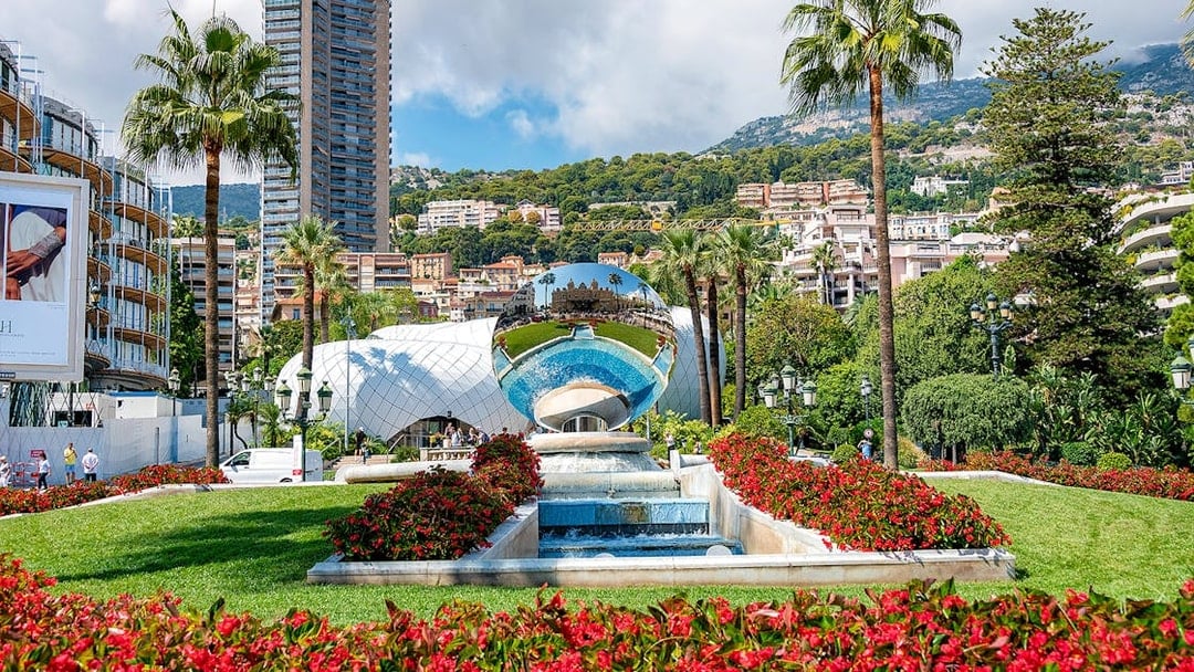 Monaco Casino Gardens with reflective sculpture and palm trees.