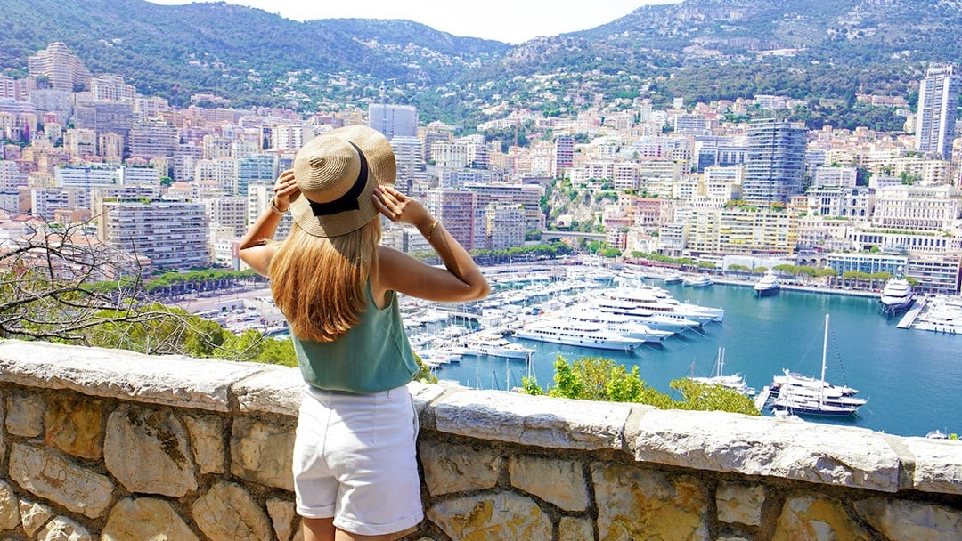 Girl overlooking Monte Carlo harbor with yachts and cityscape in view.