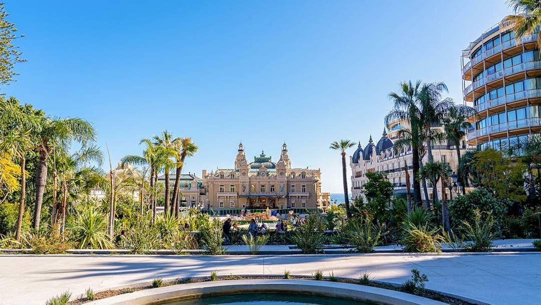 Monaco Casino with gardens and palm trees on a sunny day.