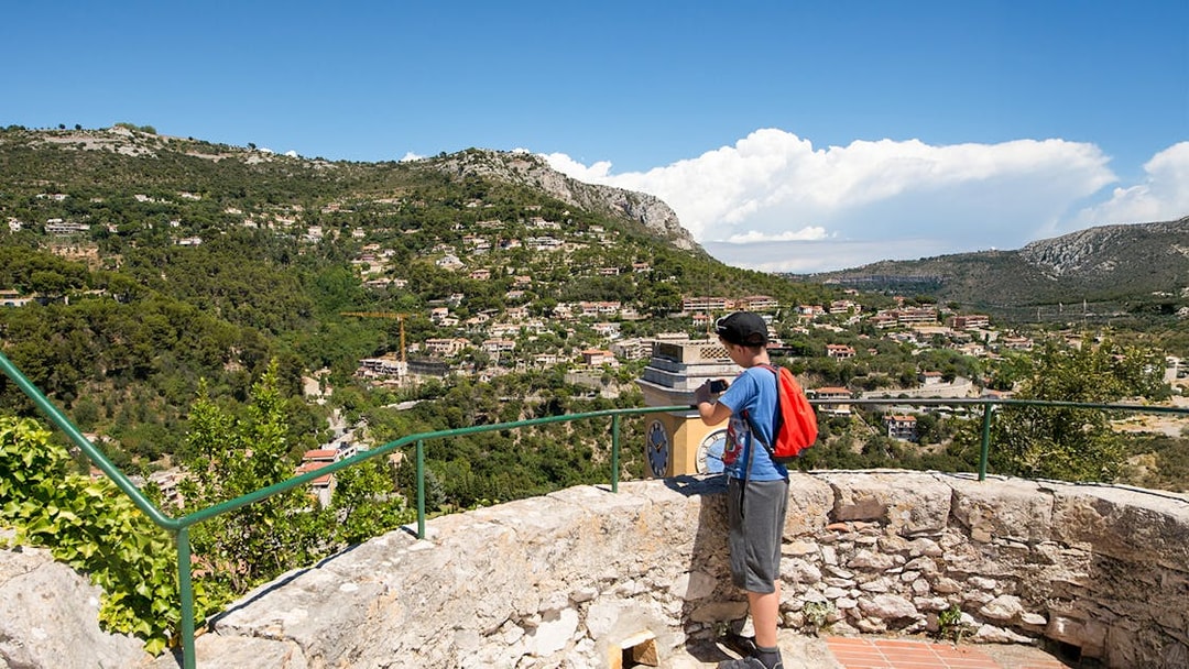 Child taking photo of Eze village landscape from a stone terrace, France.