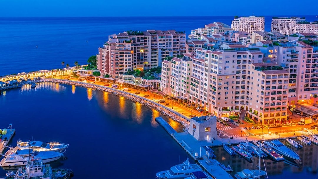 Monaco harbor at night with illuminated buildings and yachts.