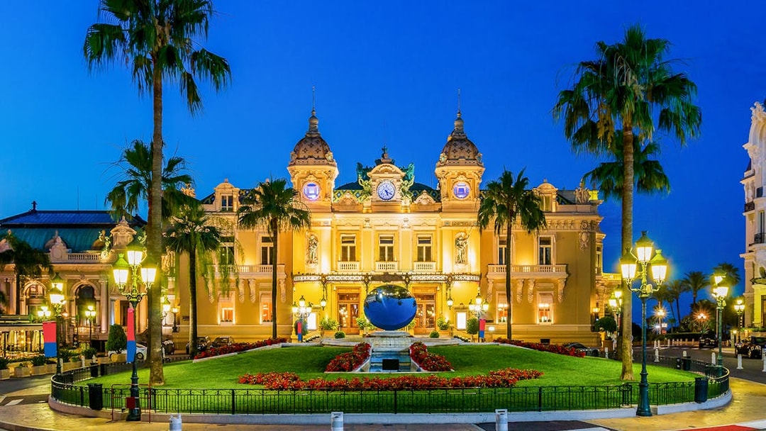 Monaco Casino illuminated at night with palm trees and gardens in the foreground.