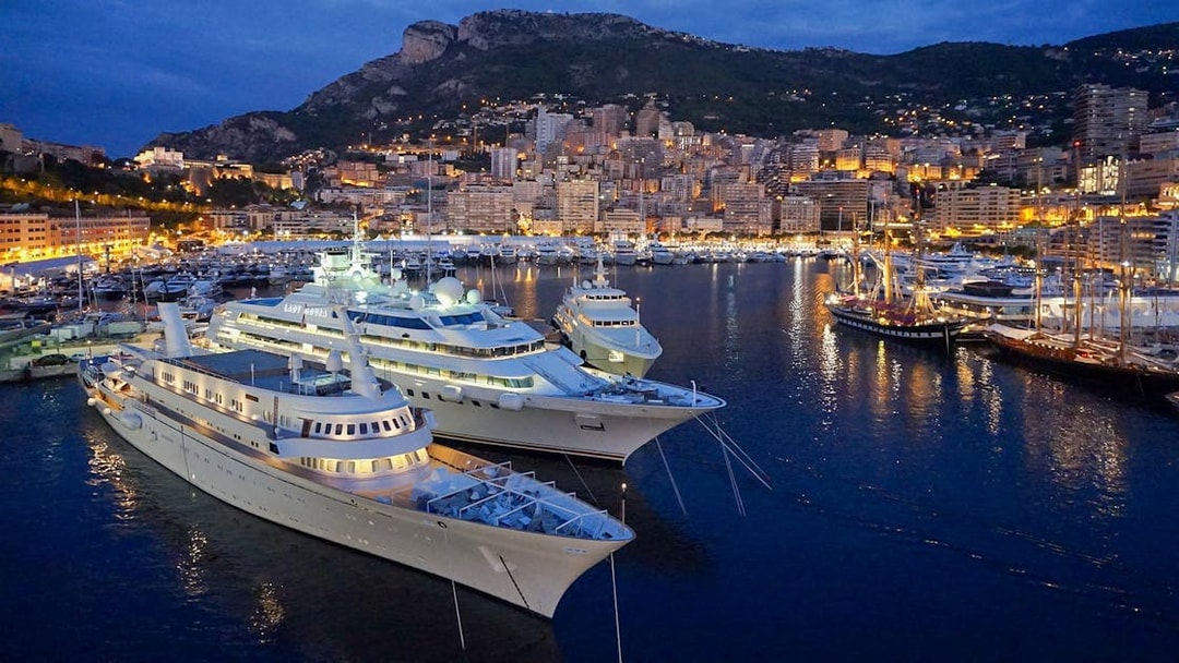 Monaco harbor at night with illuminated yachts and city skyline.