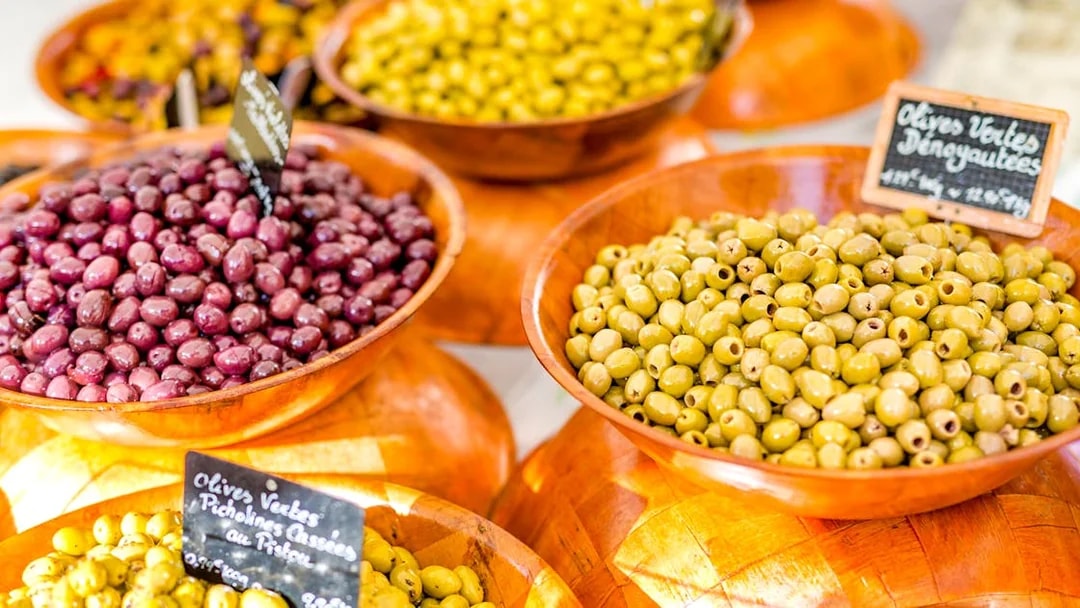Bowls of green and purple olives at a Provencal market during a wine tasting sightseeing tour.