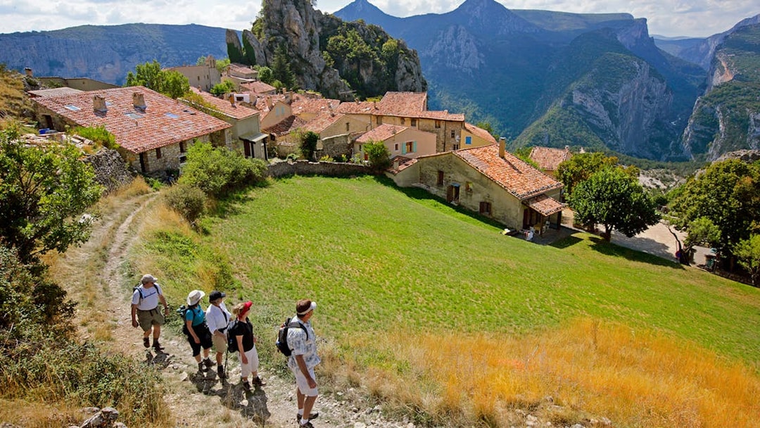 Hikers walking through a village with Gorges du Verdon cliffs in the background.
