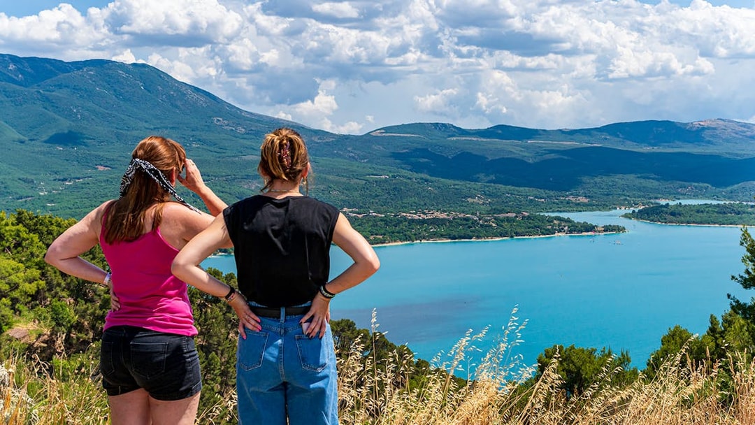Two people overlooking the Lake of St Croix in France with clear blue waters and surrounding mountains.