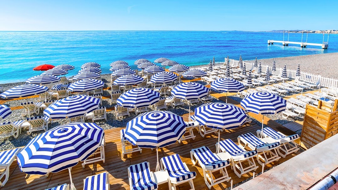 Striped umbrellas and sun loungers on a beach in St Tropez, part of the Nice to Port Grimaud day tour.